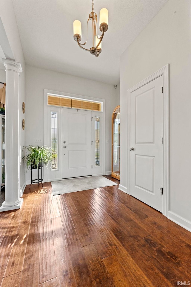 foyer entrance with wood-type flooring, an inviting chandelier, and ornate columns