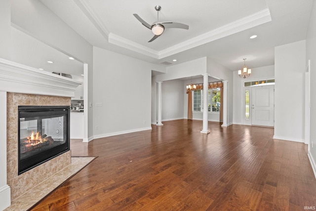 unfurnished living room with a raised ceiling, decorative columns, a high end fireplace, and ceiling fan with notable chandelier