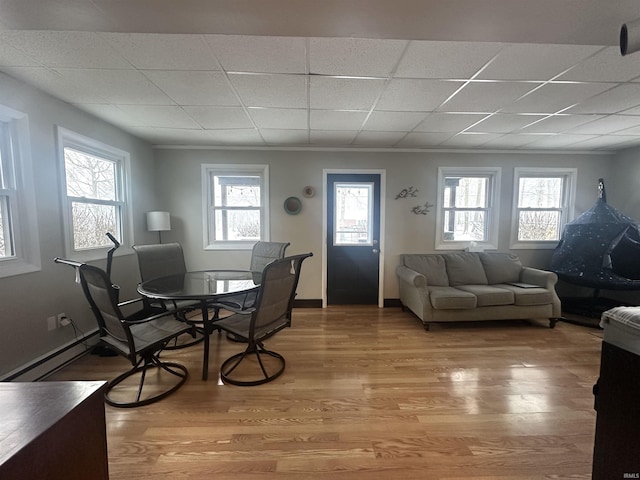 dining space featuring a paneled ceiling, wood-type flooring, a wealth of natural light, and a baseboard heating unit