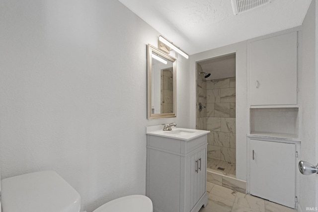 bathroom featuring a tile shower, vanity, and toilet