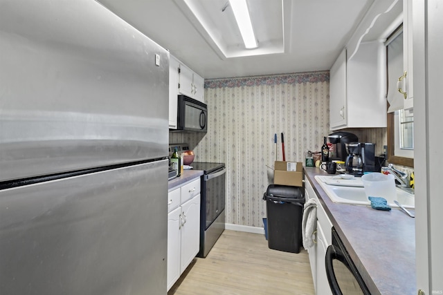kitchen featuring black appliances, light wood-style flooring, a sink, white cabinets, and wallpapered walls