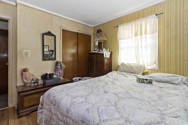 bedroom with a closet, wood finished floors, crown molding, and wallpapered walls