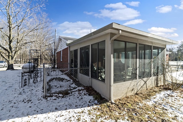 view of snowy exterior with fence, brick siding, and a sunroom