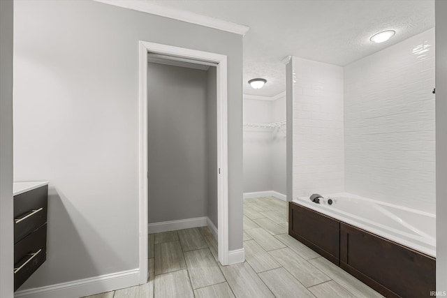 bathroom with a tub to relax in, crown molding, vanity, and a textured ceiling