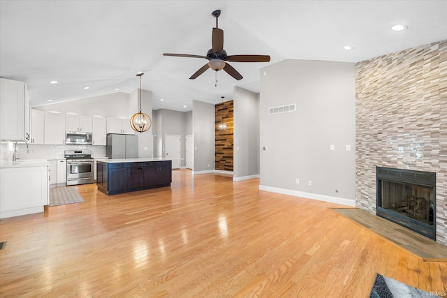 unfurnished living room featuring a fireplace, ceiling fan with notable chandelier, lofted ceiling, and sink