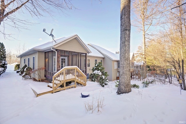 snow covered rear of property with a sunroom