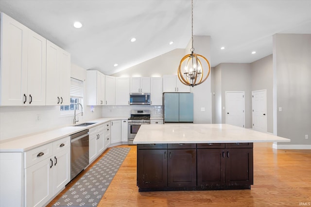 kitchen with appliances with stainless steel finishes, sink, pendant lighting, white cabinets, and a kitchen island