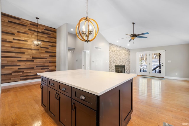 kitchen featuring dark brown cabinets, ceiling fan with notable chandelier, decorative light fixtures, a fireplace, and wood walls