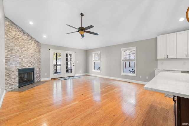 unfurnished living room featuring vaulted ceiling, light hardwood / wood-style flooring, a stone fireplace, and ceiling fan