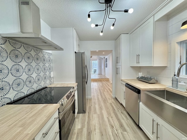 kitchen with white cabinets, a textured ceiling, stainless steel appliances, and range hood