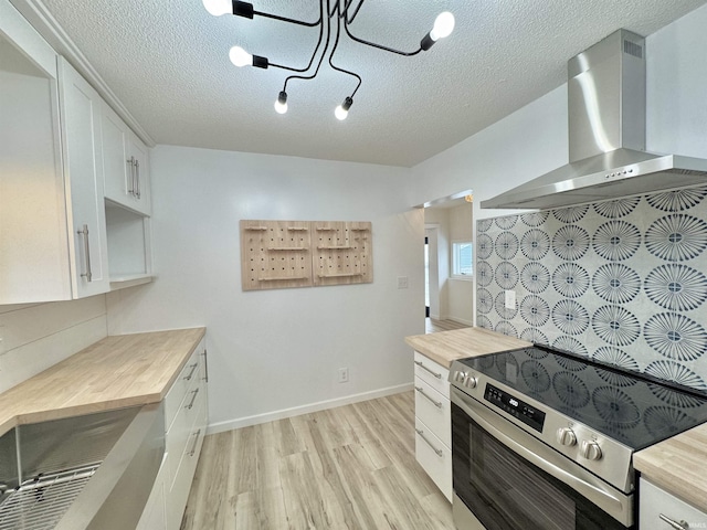 kitchen featuring a textured ceiling, white cabinetry, stainless steel range with electric stovetop, and wall chimney exhaust hood