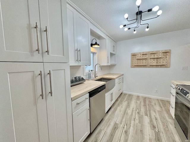 kitchen featuring appliances with stainless steel finishes, sink, pendant lighting, white cabinetry, and butcher block counters