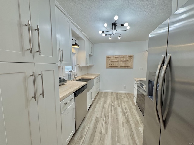 kitchen with wood counters, appliances with stainless steel finishes, a textured ceiling, decorative light fixtures, and white cabinetry