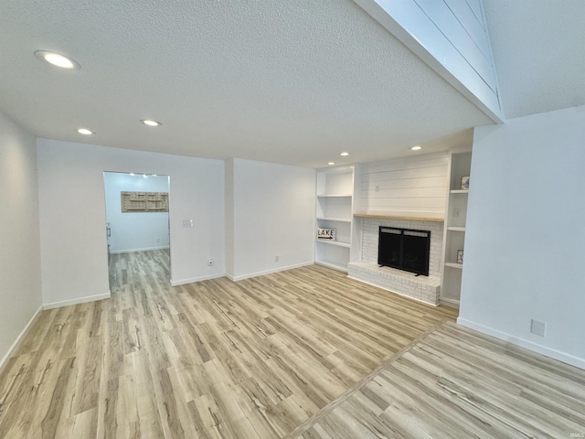 unfurnished living room featuring built in shelves, a textured ceiling, light hardwood / wood-style floors, and a brick fireplace