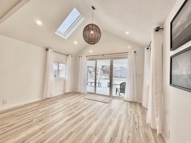 unfurnished room featuring lofted ceiling with skylight, light hardwood / wood-style floors, and a textured ceiling