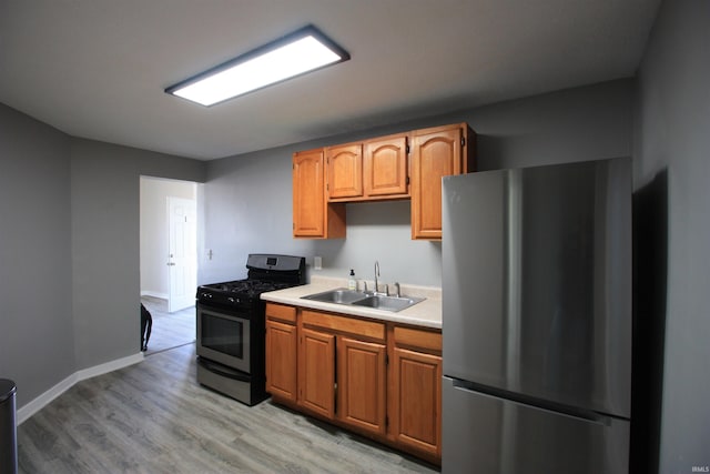 kitchen with black range with gas stovetop, stainless steel fridge, sink, and light wood-type flooring