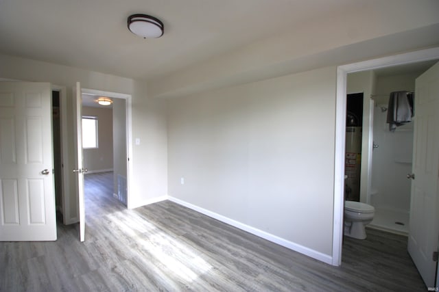 unfurnished bedroom featuring ensuite bath, water heater, and hardwood / wood-style flooring