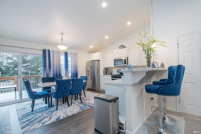 kitchen with light stone counters, stainless steel appliances, pendant lighting, white cabinetry, and lofted ceiling