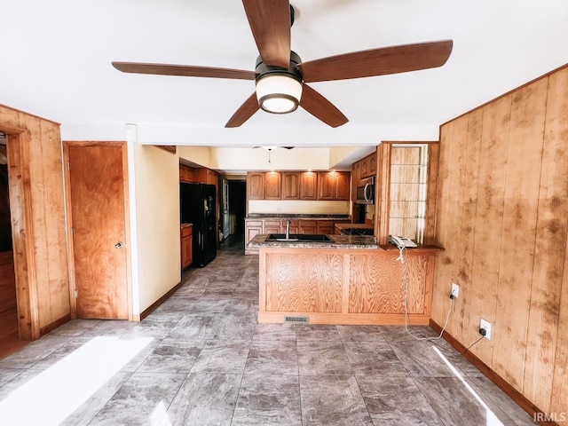 kitchen featuring black refrigerator, sink, wooden walls, ceiling fan, and kitchen peninsula