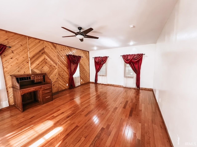 unfurnished living room featuring wood-type flooring, ceiling fan, and wood walls