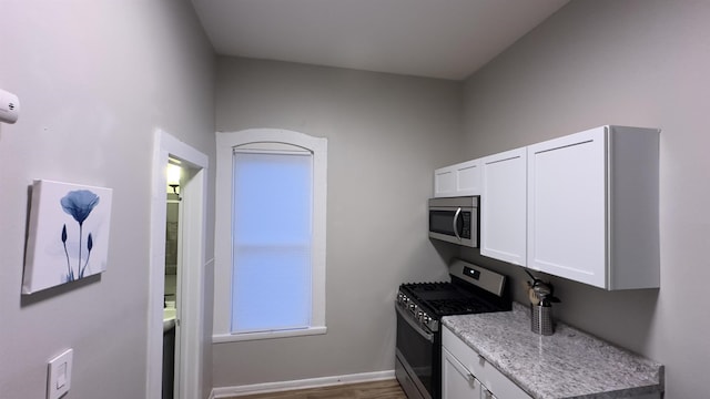 kitchen featuring white cabinets, light stone countertops, wood-type flooring, and stainless steel appliances