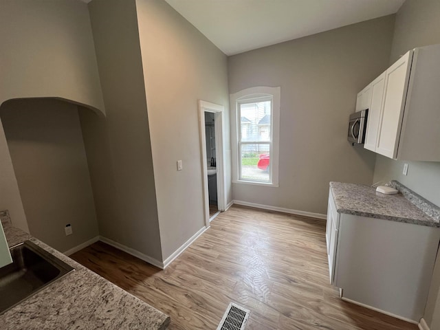 kitchen with white cabinets, light hardwood / wood-style flooring, light stone countertops, and sink