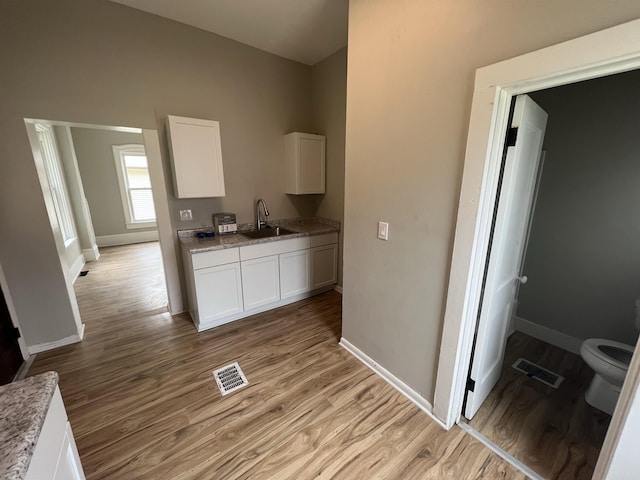 kitchen featuring white cabinetry, sink, light stone countertops, and light wood-type flooring