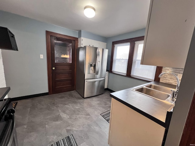 kitchen featuring stainless steel fridge, stove, white cabinetry, and sink