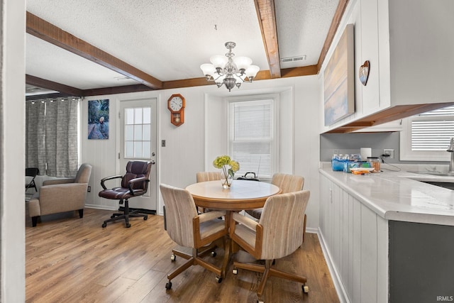 dining room with beamed ceiling, a notable chandelier, wood-type flooring, and a textured ceiling