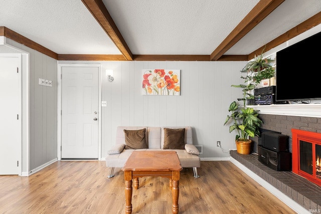 living area with hardwood / wood-style floors, wood walls, a fireplace, a textured ceiling, and beamed ceiling