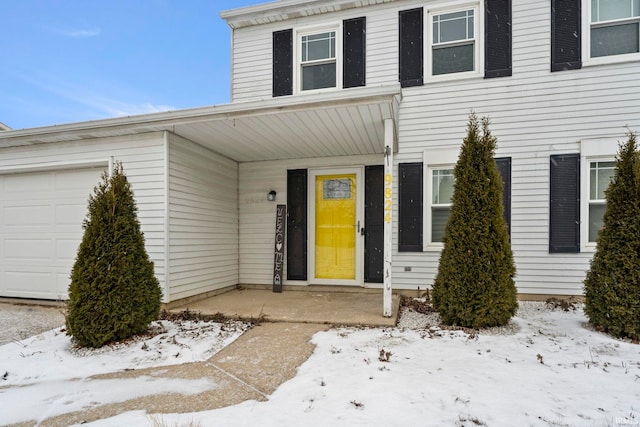 snow covered property entrance with covered porch and a garage