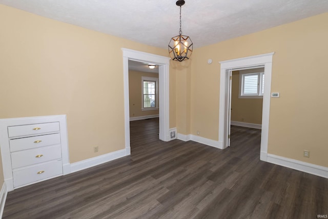 unfurnished room featuring plenty of natural light, dark wood-type flooring, and a notable chandelier