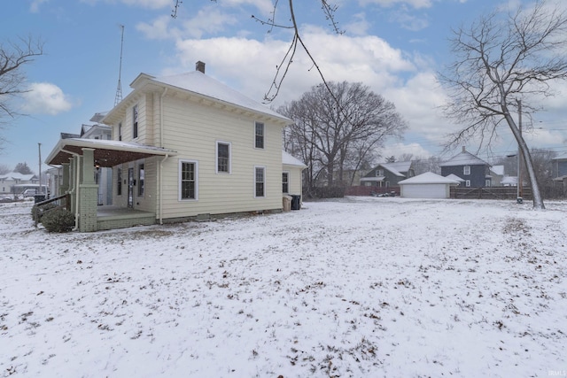 snow covered property with a garage, covered porch, and an outdoor structure