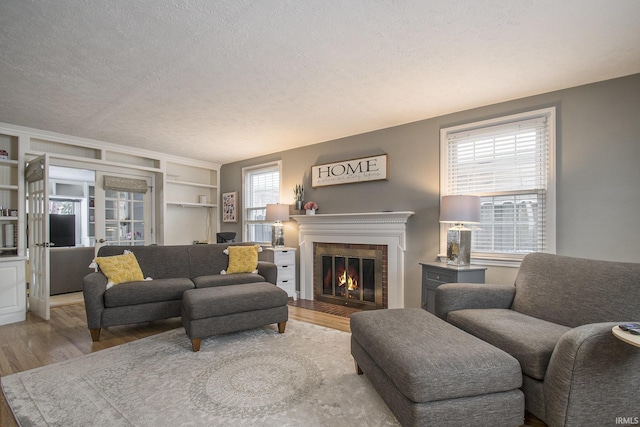 living room featuring a fireplace, built in shelves, a textured ceiling, and hardwood / wood-style flooring