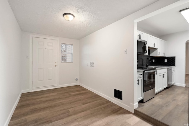 kitchen with hardwood / wood-style floors, backsplash, stainless steel appliances, and white cabinetry