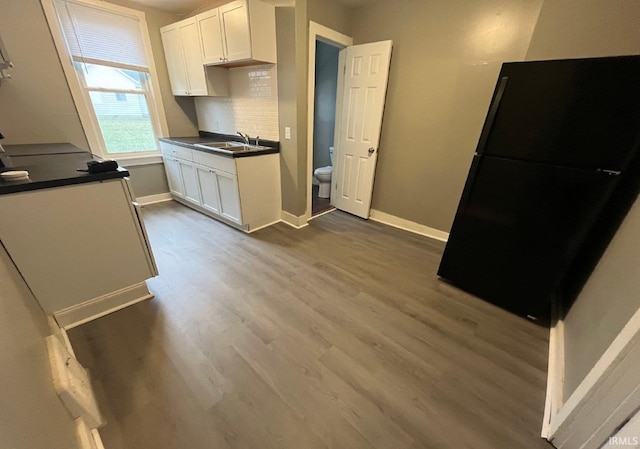 kitchen featuring backsplash, black fridge, sink, wood-type flooring, and white cabinetry