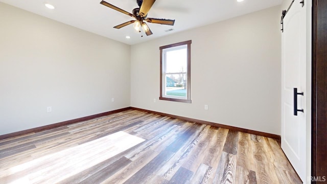 unfurnished bedroom with a barn door, baseboards, visible vents, and light wood finished floors