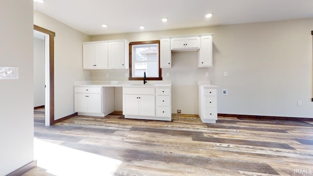 kitchen featuring baseboards, light wood finished floors, recessed lighting, a sink, and white cabinetry