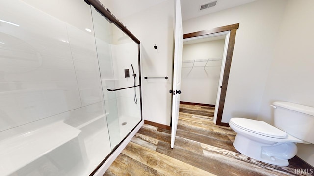 bathroom with a spacious closet, visible vents, a shower stall, toilet, and wood finished floors