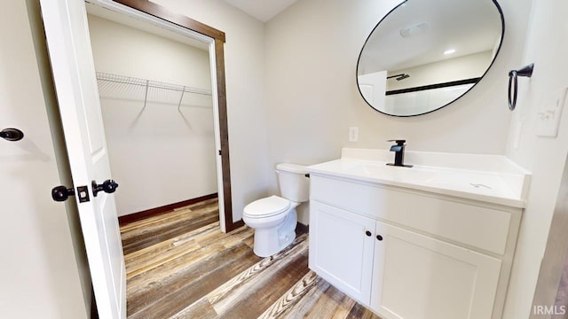 bathroom with vanity, wood finished floors, baseboards, a spacious closet, and toilet