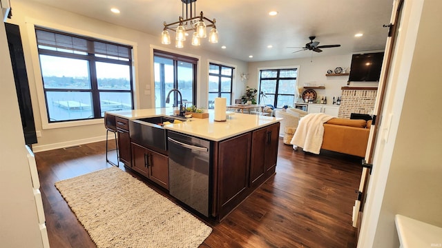 kitchen featuring stainless steel dishwasher, pendant lighting, a kitchen island with sink, dark brown cabinets, and ceiling fan with notable chandelier