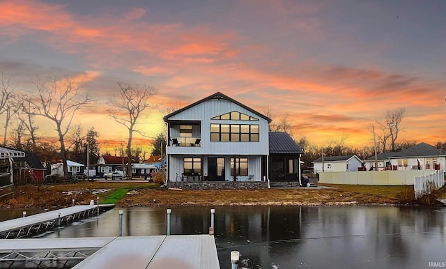 back house at dusk featuring a balcony and a water view