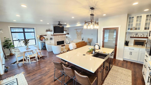 kitchen featuring white cabinetry, sink, ceiling fan, hanging light fixtures, and an island with sink