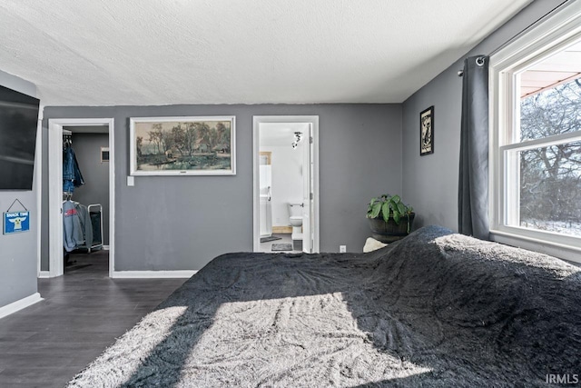 bedroom with a textured ceiling, dark wood-type flooring, and connected bathroom