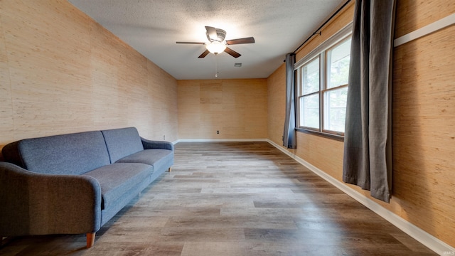 sitting room with hardwood / wood-style floors, ceiling fan, and wooden walls