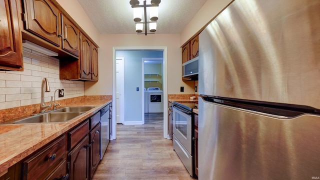 kitchen featuring sink, a textured ceiling, light hardwood / wood-style floors, washer / dryer, and stainless steel appliances