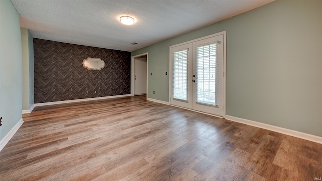 empty room featuring french doors, light wood-type flooring, and a textured ceiling