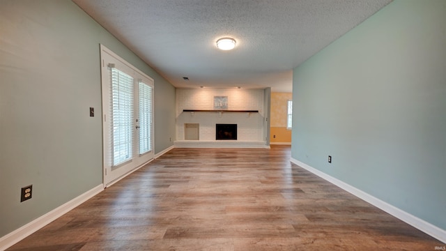 unfurnished living room featuring a wealth of natural light, hardwood / wood-style floors, a textured ceiling, and a brick fireplace