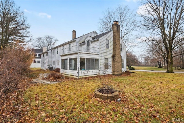 back of property with a sunroom, a fire pit, and a lawn