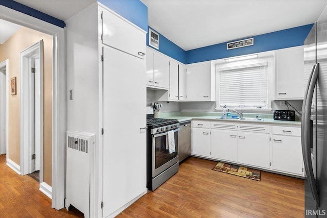 kitchen with white cabinets, sink, light wood-type flooring, appliances with stainless steel finishes, and radiator heating unit